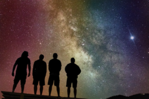 Four people's silhouettes against a colorful night sky featuring the Milky Way galaxy.