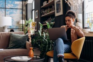 woman in brown jacket sitting on armchair while using a laptop