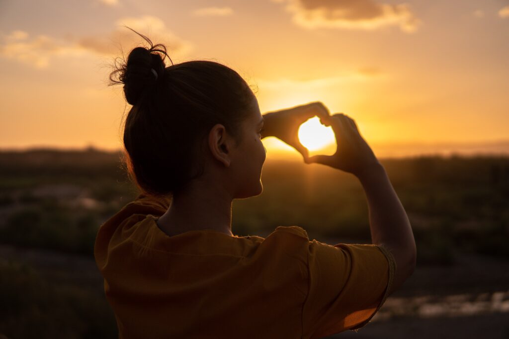 Woman making a hand heart sign over the sun