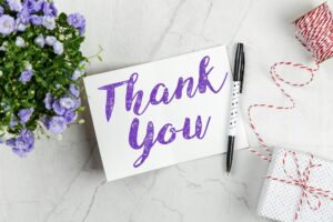 "Thank you" written in pen on a card with a gift and flowers on either side.