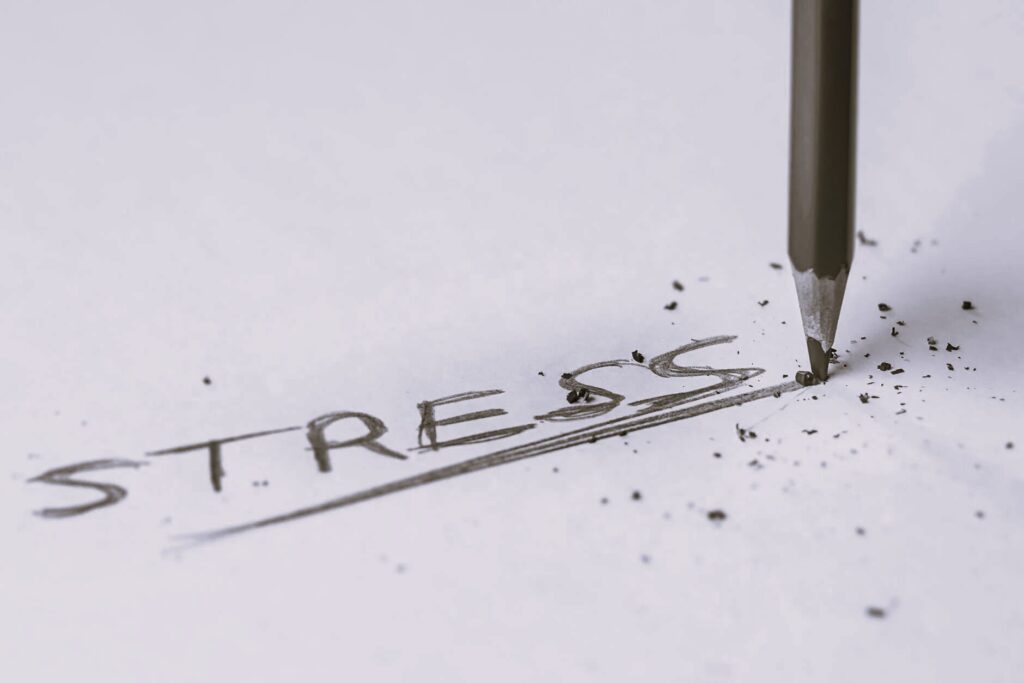 "Stress" is written on paper in all caps with several underlines. The pencil is blunt with pieces of graphite covering the page.