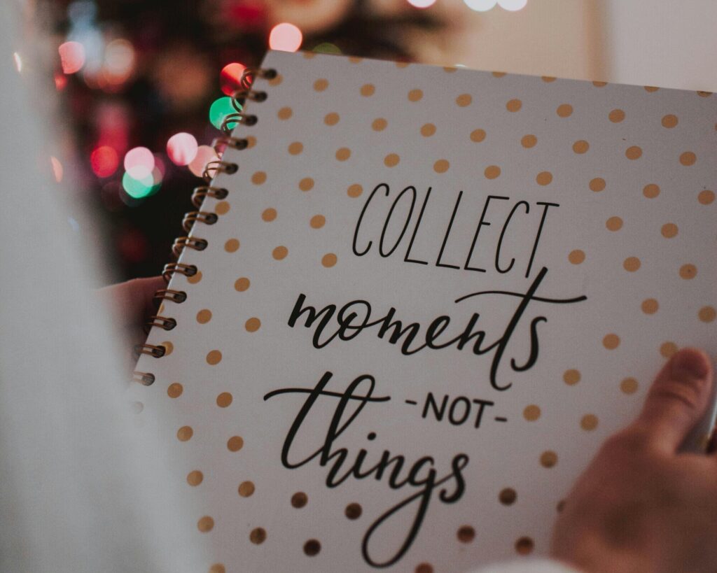 A person holds a notebook. The front of the cover says, "Collect moments not things." A christmas tree is blurred in the background.