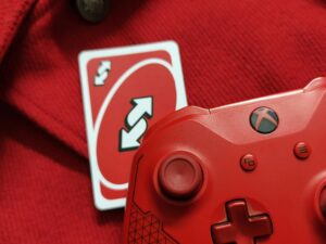 Set against a red jacket, a red Xbox controller and red Uno reverse card sit side by side.