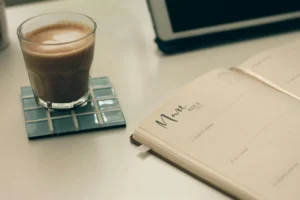 A cup of coffee and a planner sits on top of a table.