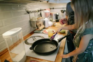 A child and mother stand by a frying pan in the kitchen.