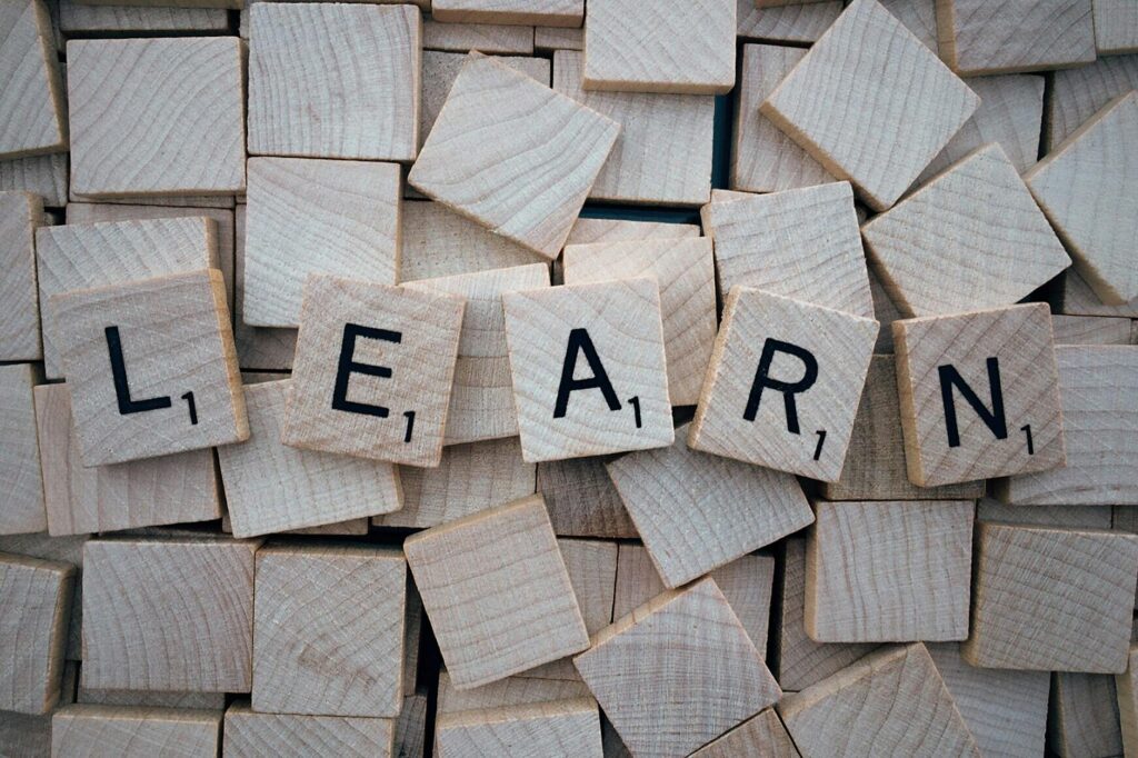 "Learn" is spelled out of scrabble letters on a pile of overturned, blank scrabble pieces.