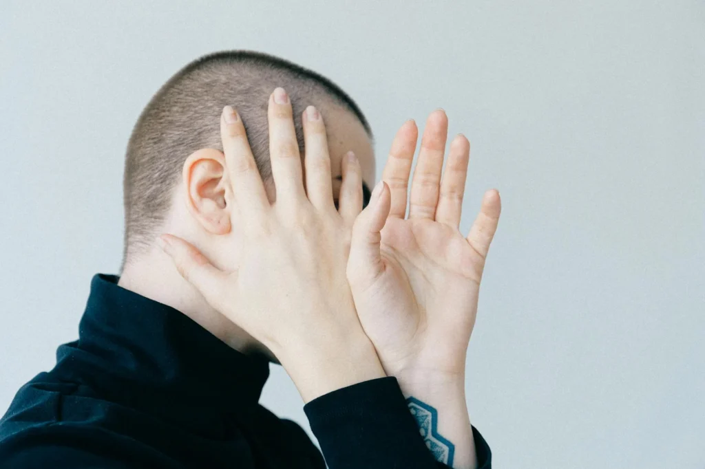 A person holds up their hands, covering their face from the camera.