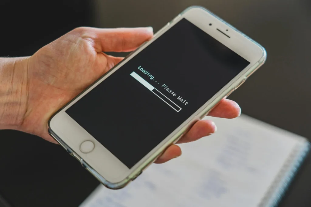 A person holds a phone up to the camera. The phone shows a progress bar with the words "Loading...Please wait".