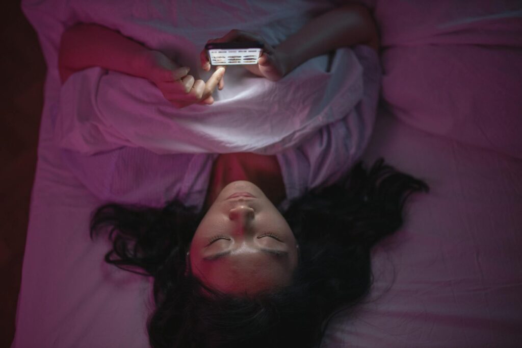 A woman lying in bed while scrolling through her phone.