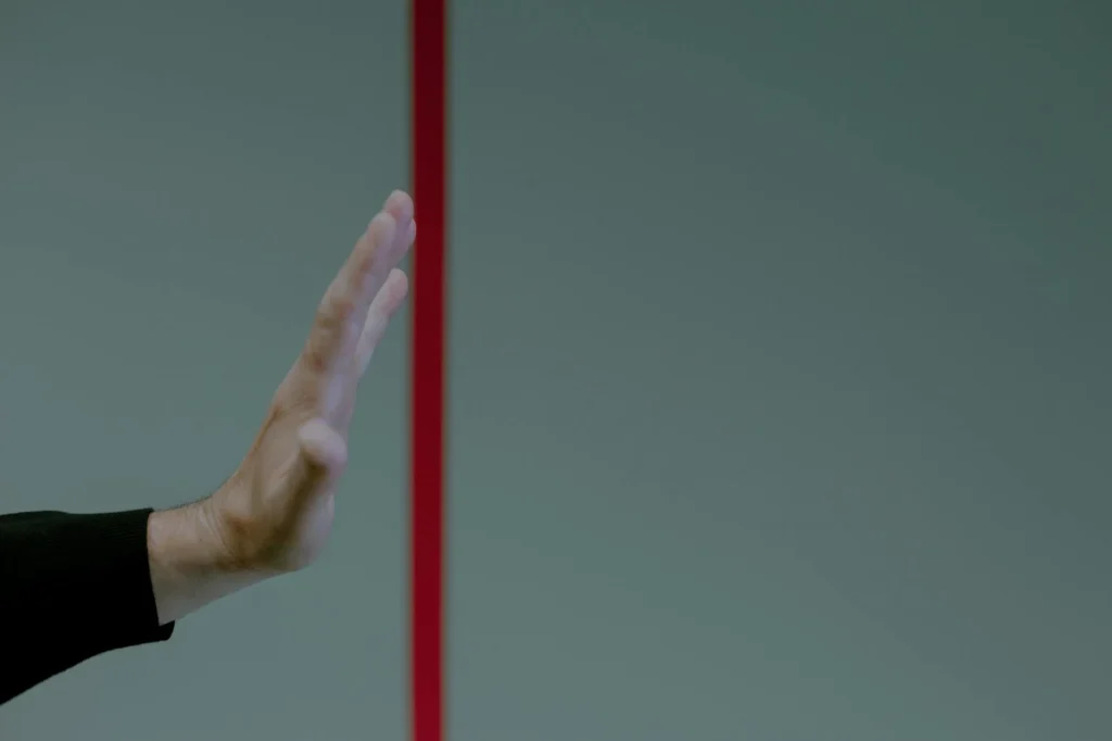 A hand reaches into frame from the left. A red line runs down the middle. The hand is held up before the red line, not crossing over.