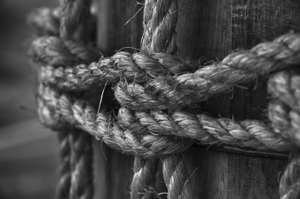 A black and white photo of a rope tied into a strong knot around a post.