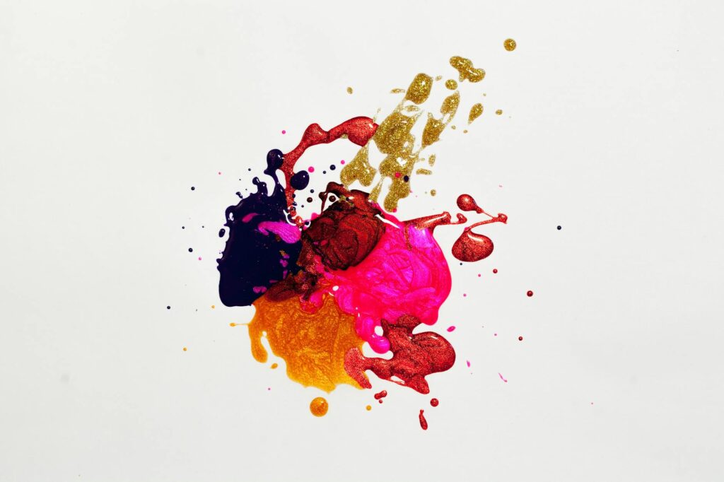 A splatter of wet paint against a white background. The colors pink, yello, black, orange, and red mix.